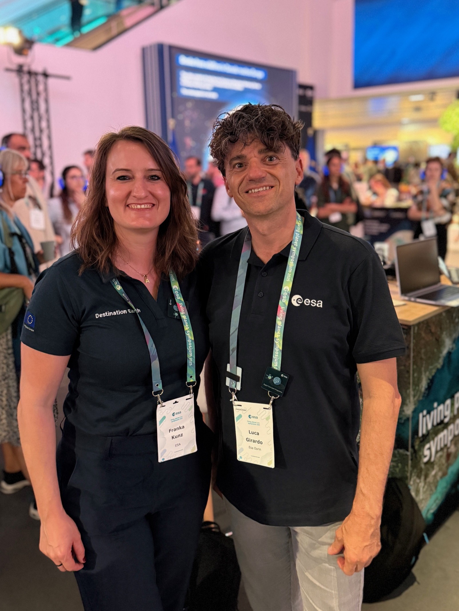 A woman (Franka Kunz) and a man (Luca Girardo) are smiling. They are in a crowded room — a poster hall within a scientific conference. Scientific posters can be seen in the background.